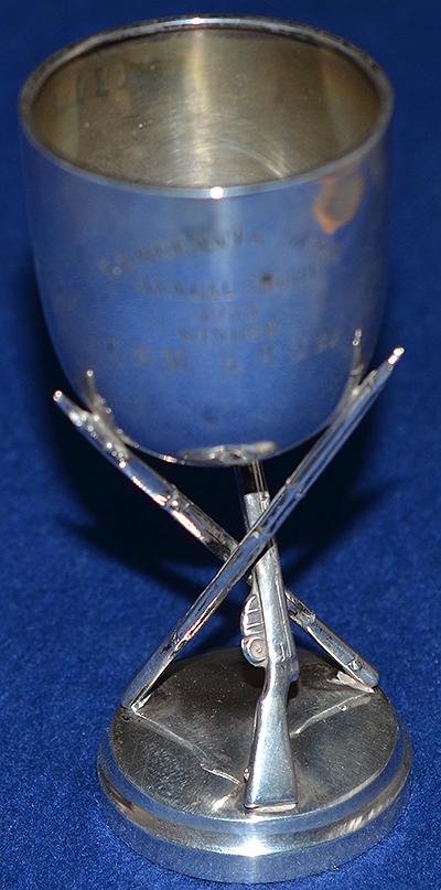 SILVER MILITARY TROPHY CUP SITTING ON THREE MILITARY RIFLES.