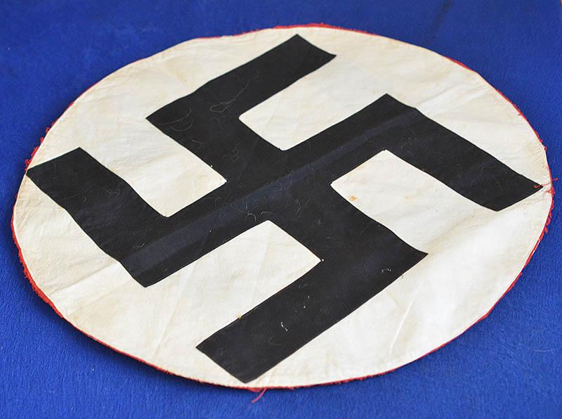 LARGE BLACK CLOTH SWASTIKA ON WHITE CIRCLE.